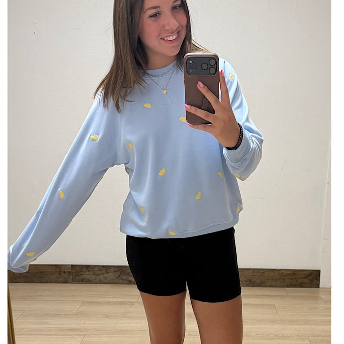Person wearing a light blue sweatshirt with yellow patterns and black shorts, taking a mirror selfie.
