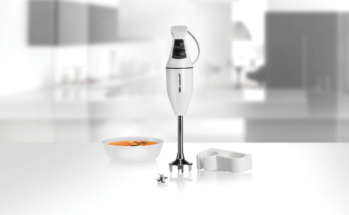 Der ESGE Zauberstab ESGE-Zauberstab 901205 Set M100 Design-Stabmixer steht aufrecht auf einer modernen Küchentheke neben einer Schüssel Suppe, einem Mixmesser und einem weißen Kunststoffaufsatz mit sanft verschwommenem Hintergrund.