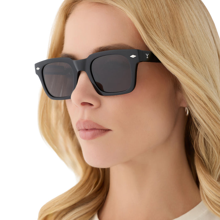 on model - female wearing yellowstone x diff eyewear featuring the kayce dutton square sunglasses with a classic black acetate frame and grey polarized lenses angled view
