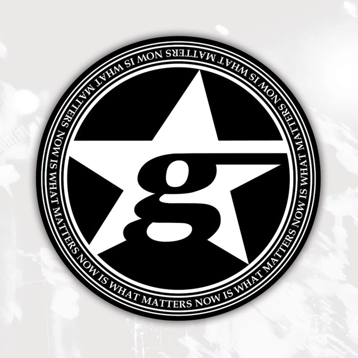 A black and white circular Gameface logo coaster with a large star and lowercase “g” in the center. The border repeats "NOW IS WHAT MATTERS" in all caps, making it a stylish choice for your drinks.