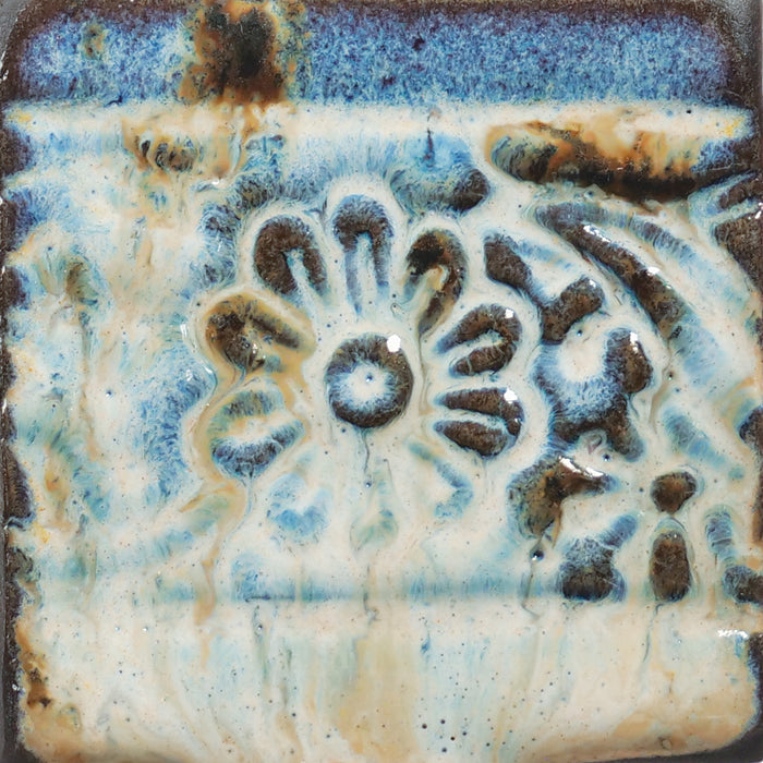 Embossed square test tile in Amaco PCF-74 River Birch glaze, cream breaking to blue and dark brown over a flower relief
