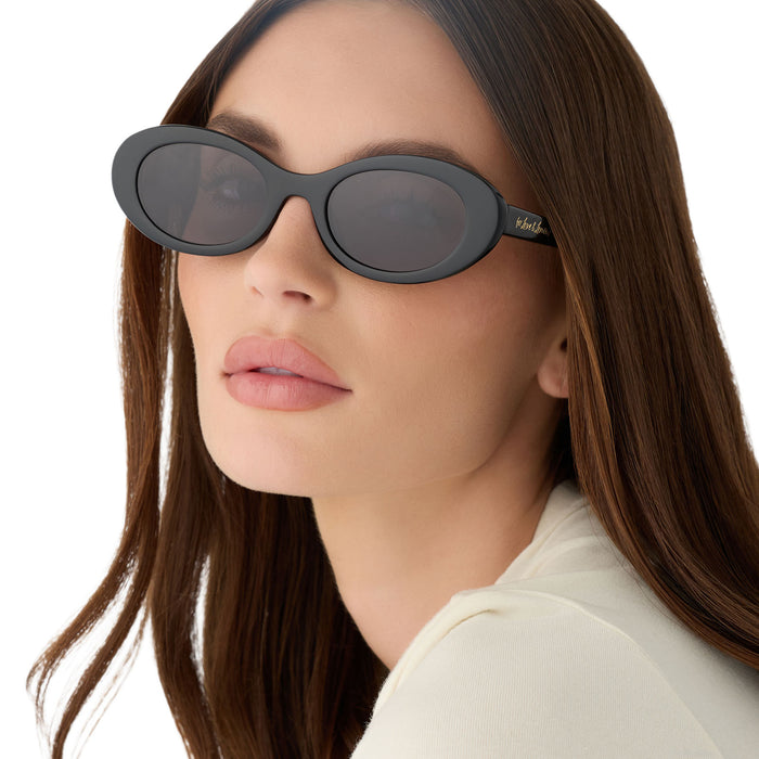 on model - female wearing for love & lemons x diff eyewear featuring the sabrina oval sunglasses with a black acetate frame and grey polarized lenses angled view