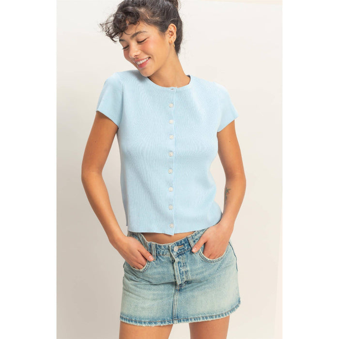 Woman wearing a light blue top and denim skirt against a plain background