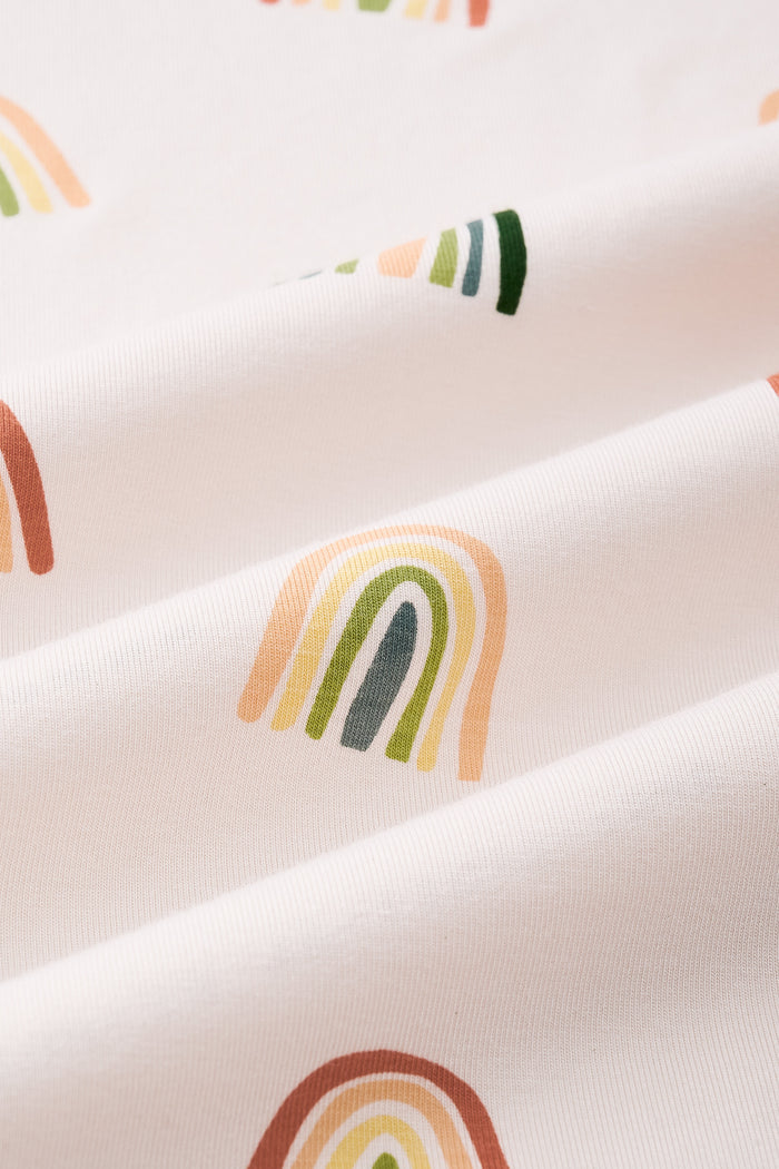An all-over print featuring alternating rows of boho style rainbows in alternating directions over a light beige background color called Vanilla.
One row of rainbows has an outermost arc colored in a dark cool green, followed by a cool sage green, then a light olive green, and finished with an inner core colored in a light apricot.
Another row of of rainbows has an outermost arc colored in a burnt orange called Apricot, followed by a light peach, then a light yellow called Lilikoi, and finis