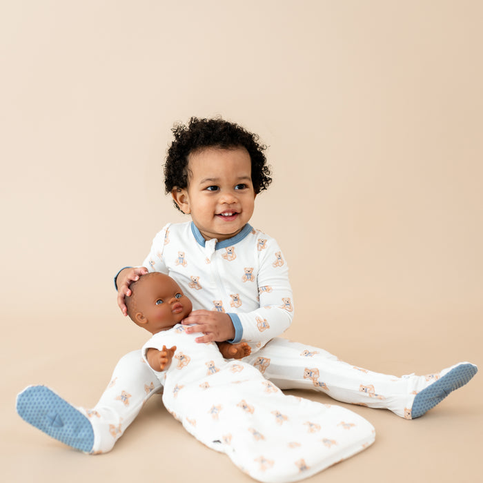 Little boy in Zippered Footie in Teddy Bear holding a baby doll wearing Baby Doll Sleep Bag in Teddy Bear