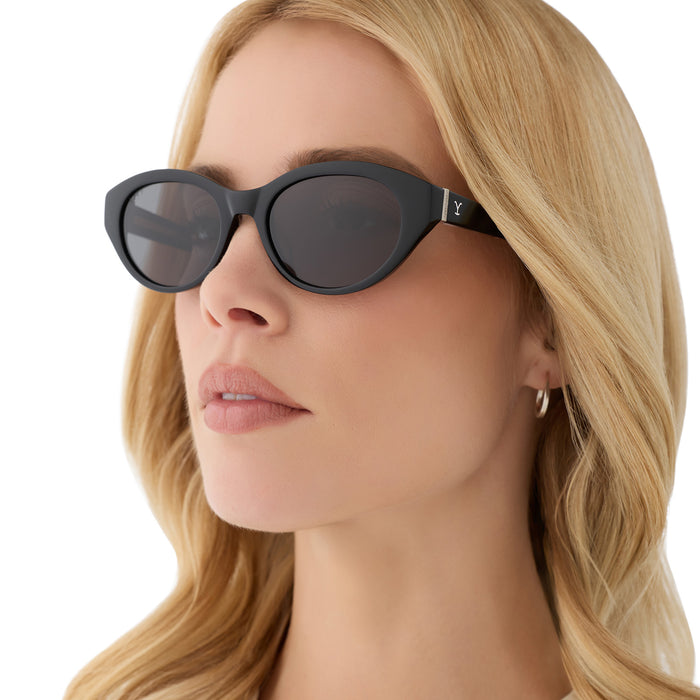 on model - blonde female wearing yellowstone x diff eyewear featuring the teeter round sunglasses with a classic black acetate frame and grey polarized lenses angled view