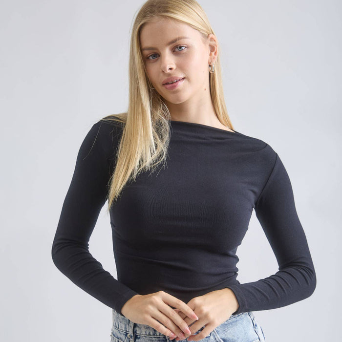 Woman wearing a black long-sleeve top and denim skirt against a plain background