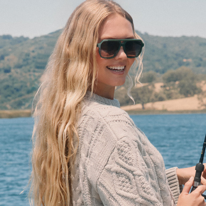 lifestyle -  blonde female fishing wearing diff eyewear featuring the cameron navigator sunglasses with a fairway green acetate frame and grey gradient polarized lenses front view