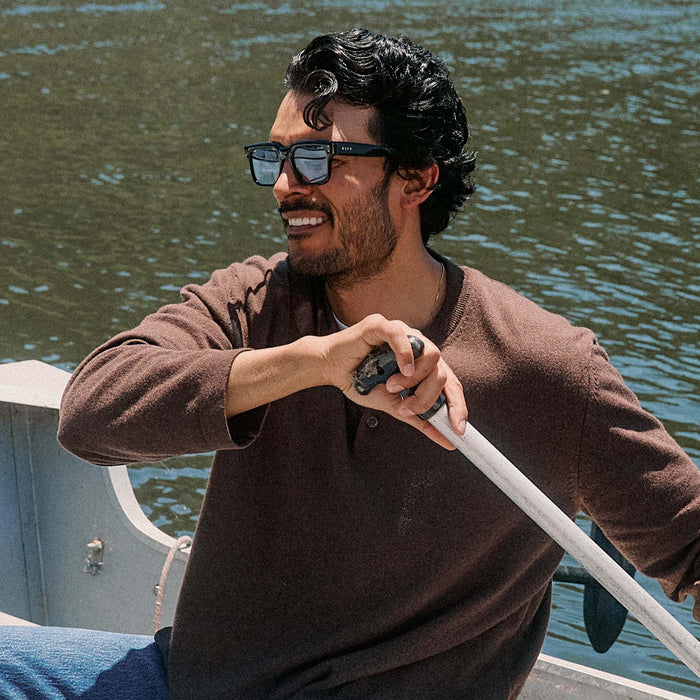 lifestyle - male on a boat wearing diff eyewear cash  sunglasses with a black acetate frame and light blue tint lenses angled view
