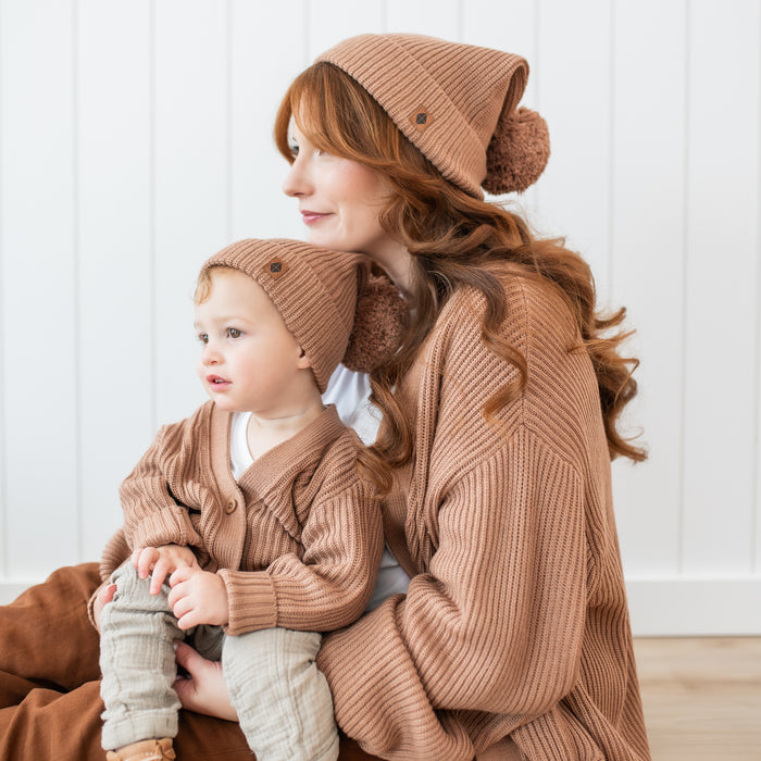 Mother wearing the Chunky Knit Adult Pom Beanie in Latte and matching chunky knit women's oversized cardigan with her son on her lap