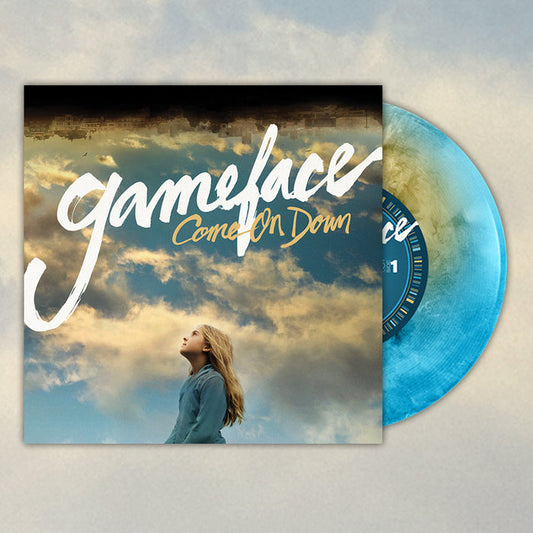 A Gameface vinyl record in striking blue and white marbled vinyl rests by its cover, which shows a blonde woman gazing up at golden clouds under the album title Come On Down in bold white and yellow script.