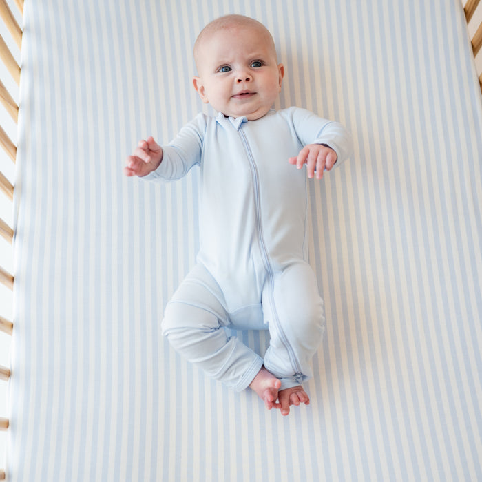 Infant wearing a Zippered Romper in Mist laying on a Crib Sheet in Small Mist Stripe