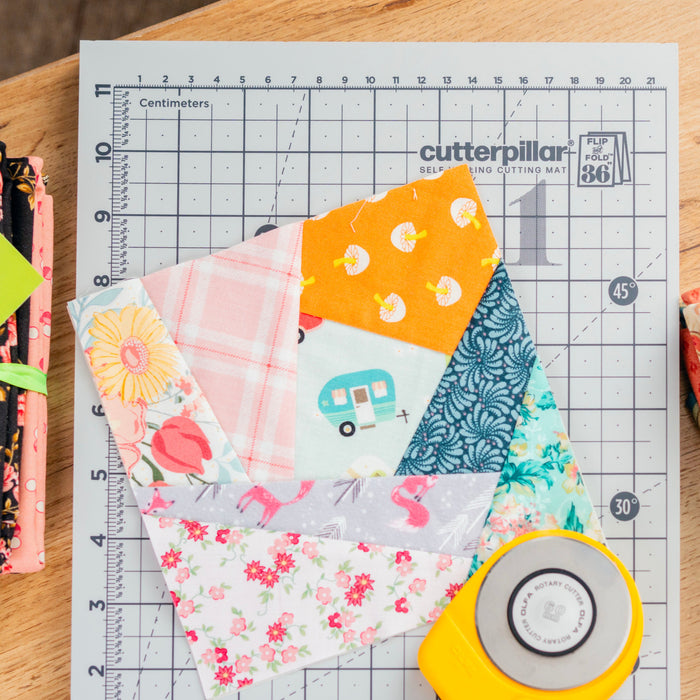 Fabric squares on a cutting mat with a rotary cutter, on a wooden surface.