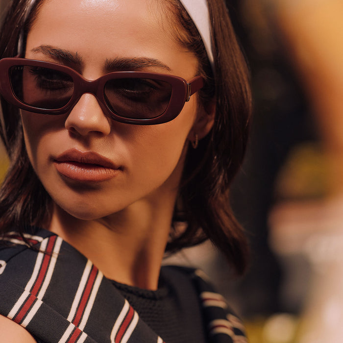 lifestyle - female wearing diff eyewear featuring the daphne rectangle sunglasses with a rugby red acetate frame and grey polarized lenses front view
