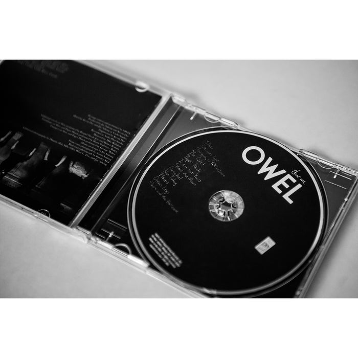 Black and white photo of an OWEL music CD in an open case, featuring the handwritten Dear Me track list on the disc and a partially visible booklet on the left. Brand: OWEL.