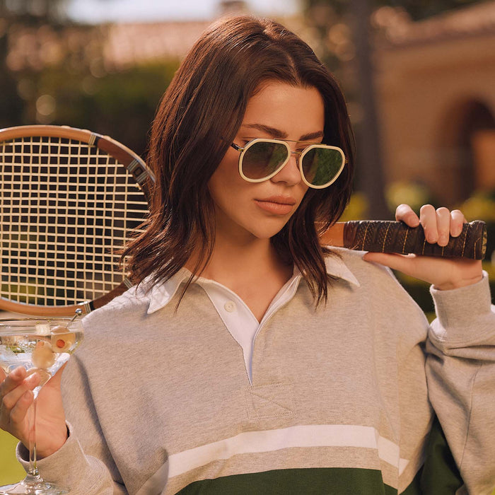 lifestyle - female after tennis match wearing diff eyewear featuring the joey round sunglasses with a courtside ivory & gold metal frame with blue slate gradient flash lenses angled view
