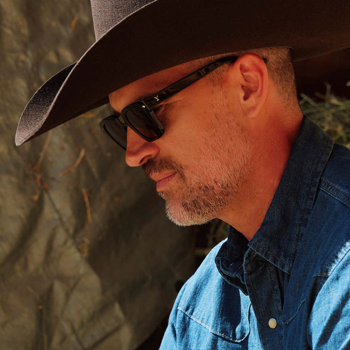 lifestyle - male cowboy wearing yellowstone x diff eyewear featuring the kayce dutton square sunglasses with a classic black acetate frame and grey polarized lenses side view