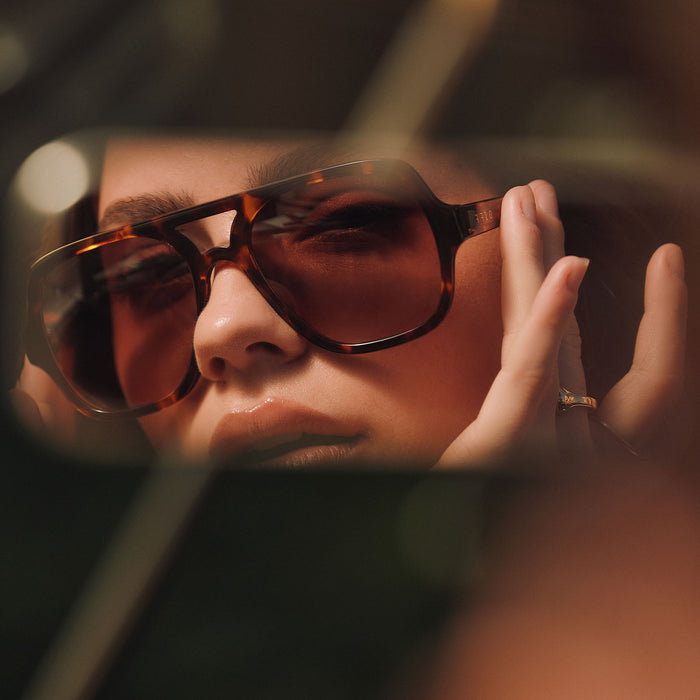 lifestyle - female looking at her rear view mirror of her car wearing on model - female wearing diff eyewear featuring the layton navigator sunglasses with a rich tortoise acetate frame and brown gradient lenses