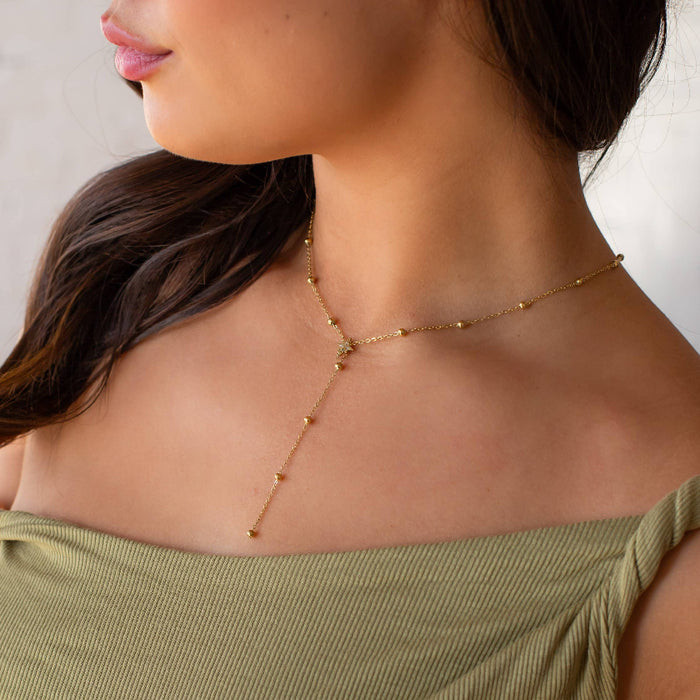 Close-up of a woman wearing a delicate gold necklace against a neutral background