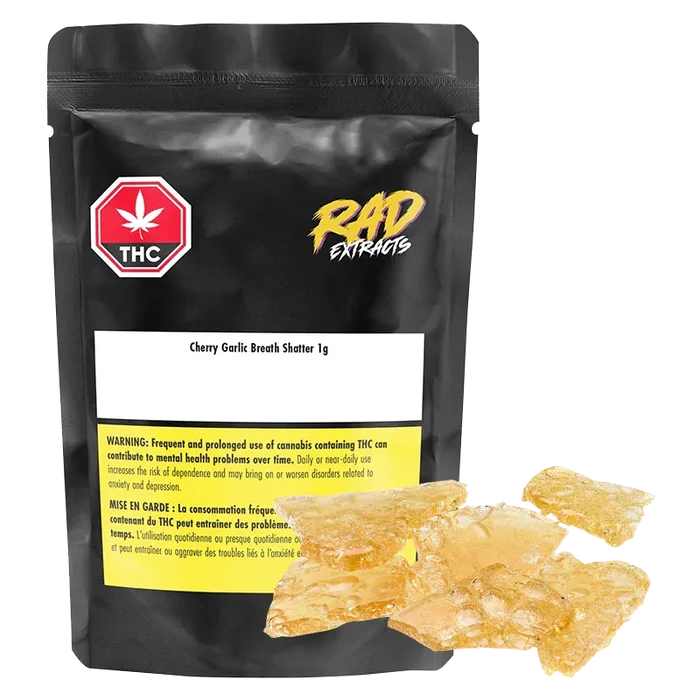Front-facing shot of a black pouch and amber glassy shards labeled Mango Kush x Galactic Giggles Shatter, the 1 g pieces gleaming against a white background