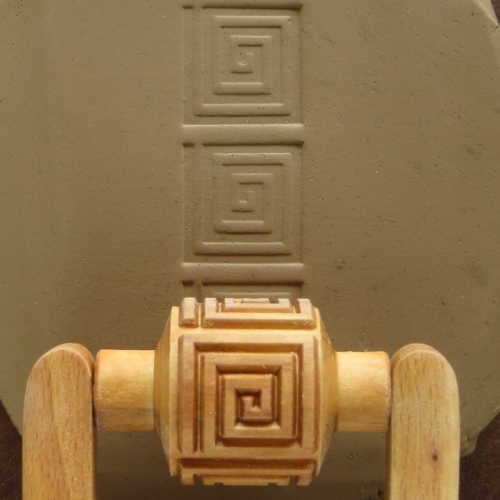 MKM Medium Handle Roller in the Square Spiral pattern, pressing a strip of square spirals into grey clay