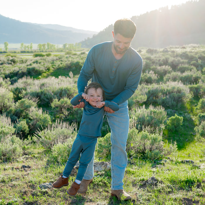 Father and son having fun in a field while matching in Atlantic. Pictured are the long sleeve todder pajamas and Men's Long Sleeve Henley Top