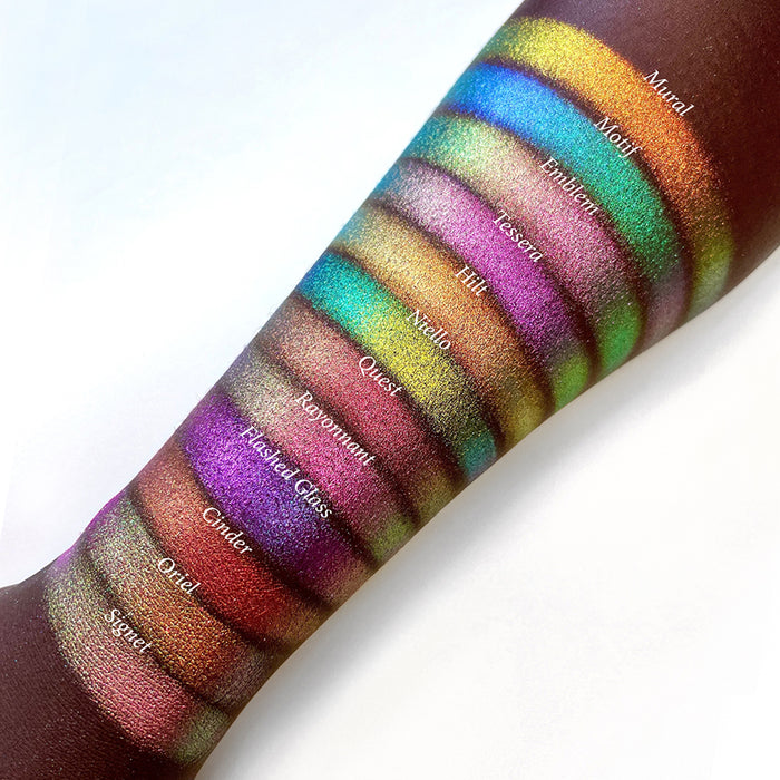 Top angled arm swatches on deep skin tone of Niello Electric Multichrome Pigment shifts compared to Mural, Motif, Emblem, Tessera, Hilt, Quest, Rayonnant, Flashed Glass, Cinder, Oriel and Signet