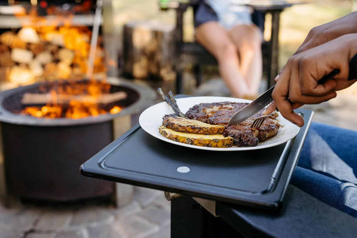 This is an image of someone eating steak on a Breeo Outrig Tray