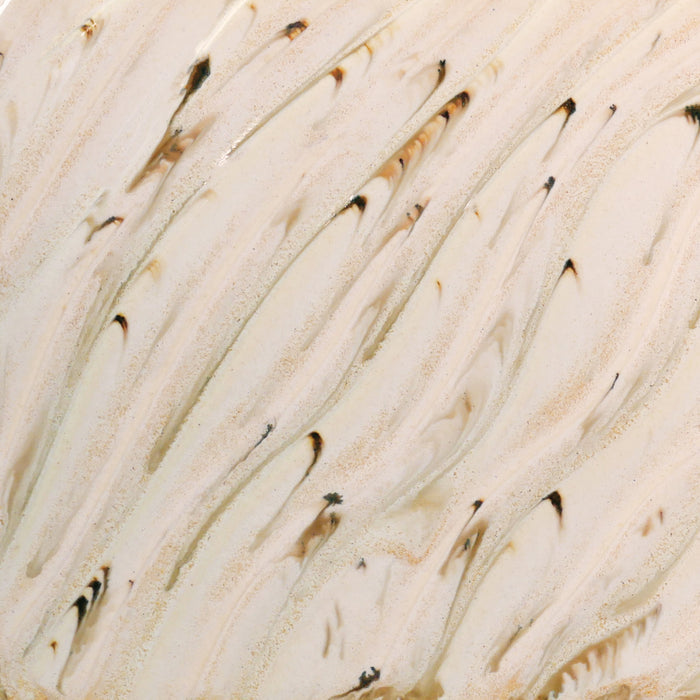 Close-up of Amaco PCF-74 River Birch glaze, glossy cream surface streaked with dark brown specks and tan runs