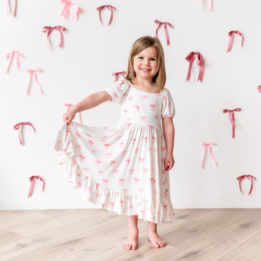 Child modeling Puff Sleeve Twirl Dress in Bow pulling bottom of dress out to show the movement of skirt