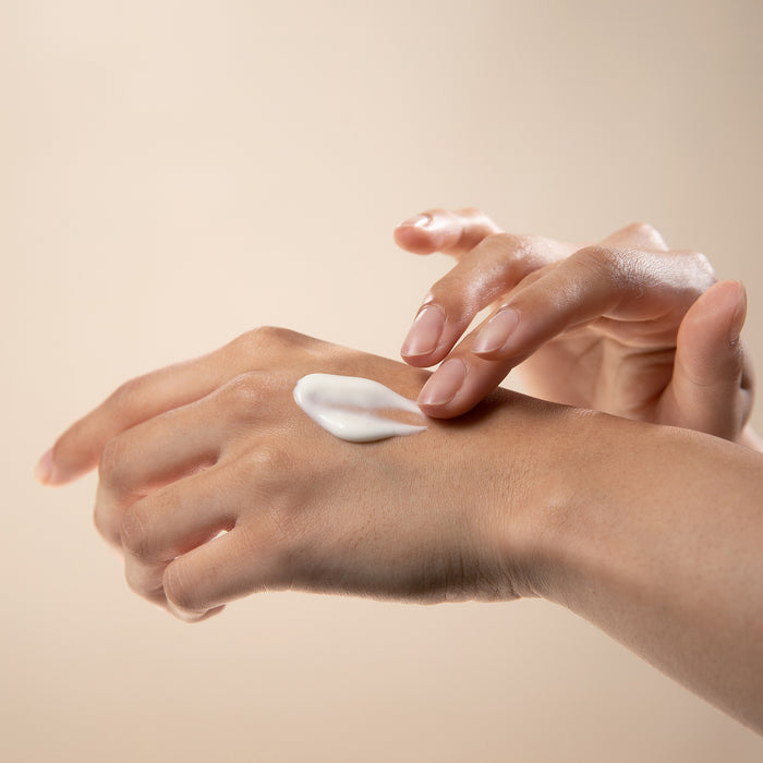 Person applying lotion to their hand against a beige background