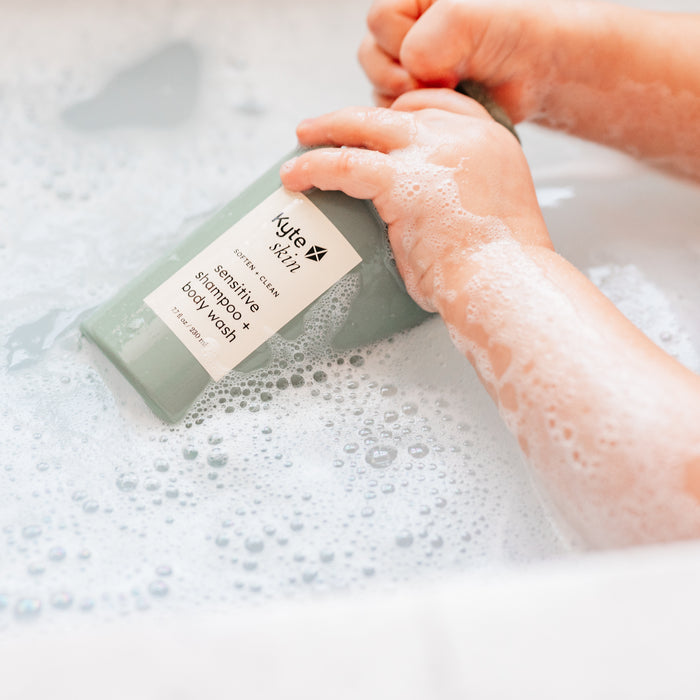 Person holding a bottle of Kyte Skincare shampoo and body wash in a bathtub filled with bubbles.