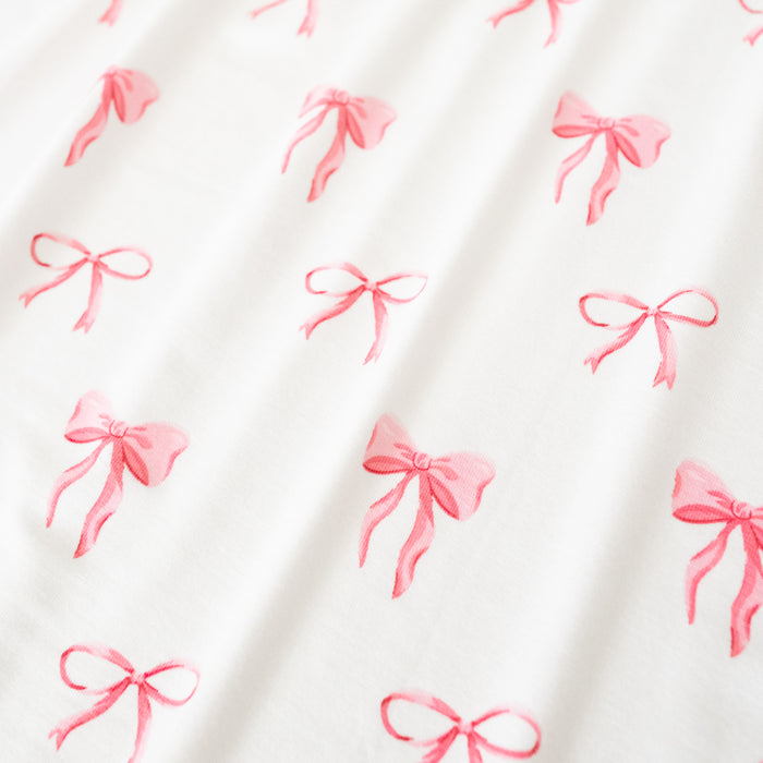 Close up of bamboo fabric: An all-over print of thin and thick light pink bows over a white background.