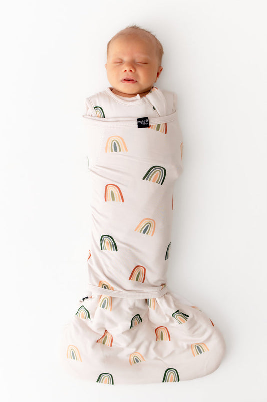 Baby sleeping in Sleep Bag Swaddler in Retro Rainbow 1.0 print on a white background