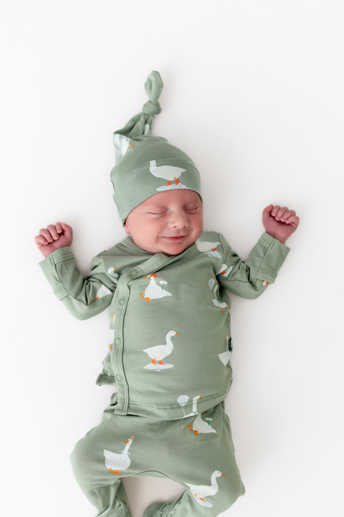 Newborn baby wearing a green outfit with silly goose pattern and matching hat on a white background
