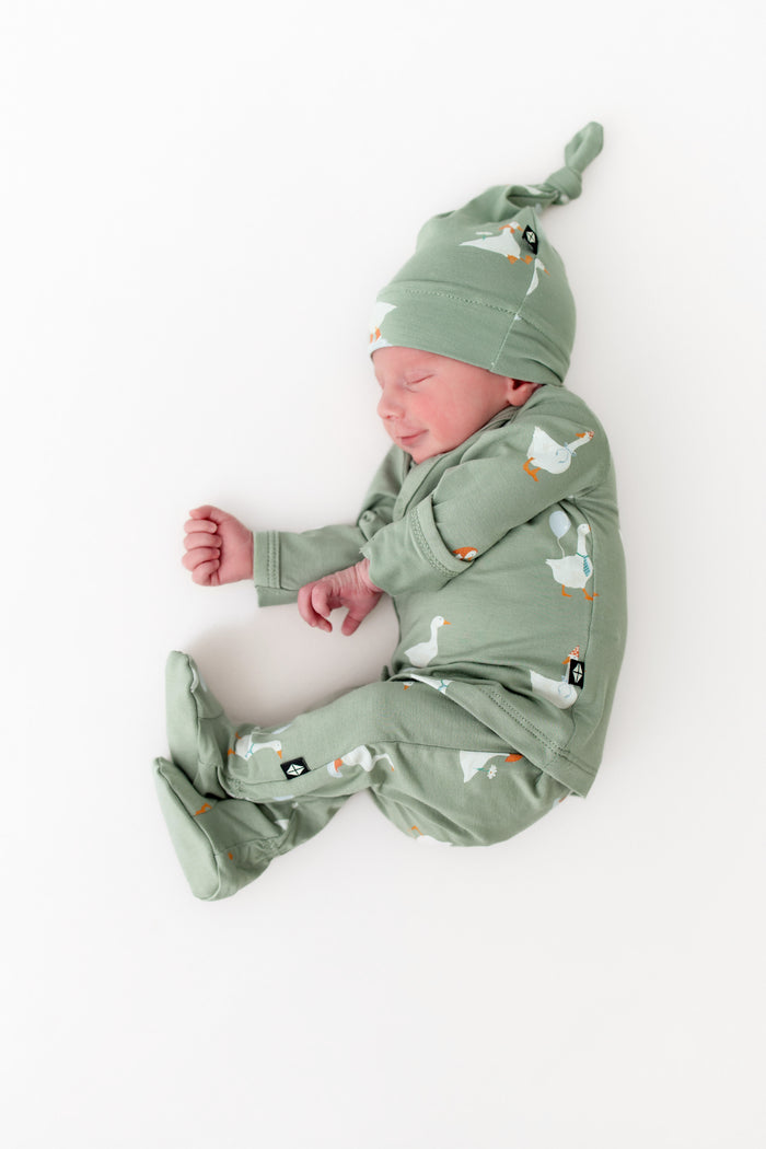 Newborn baby in a green outfit with silly goose pattern on a white background