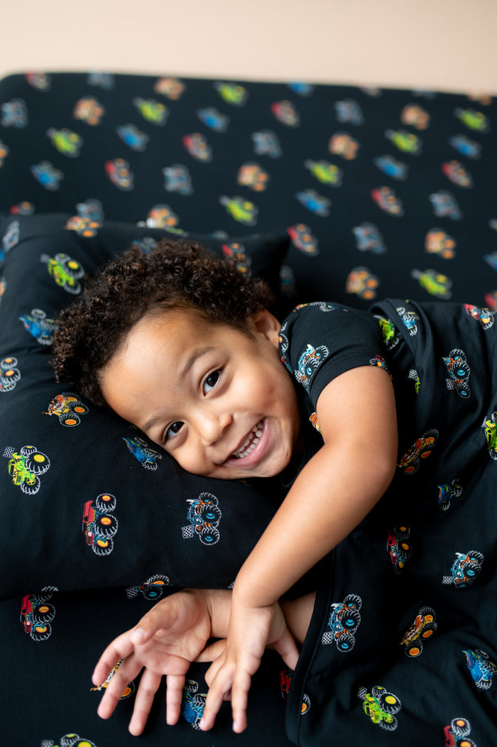 Boy lying on black Toddler pillowcase and sheet in Monster Truck print covered with similar print Toddler blanket