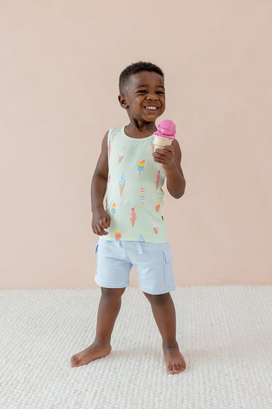 Child smiling and holding an ice cream cone wearing a Toddler Tank Top in Mint Ice Cream print over blue shorts on a beige background