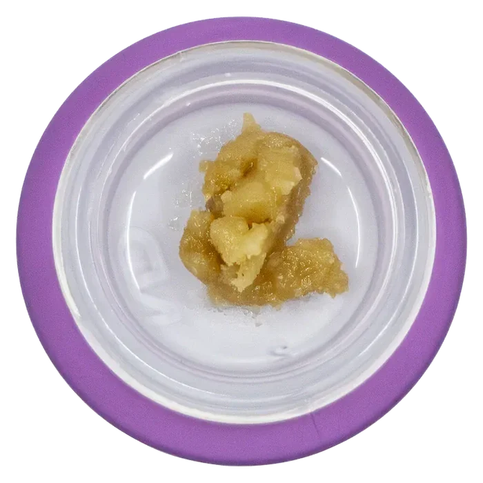 Top-down view of a pale amber concentrate in a white dish with a purple rim labeled Tropical Twist Live Resin Badder.