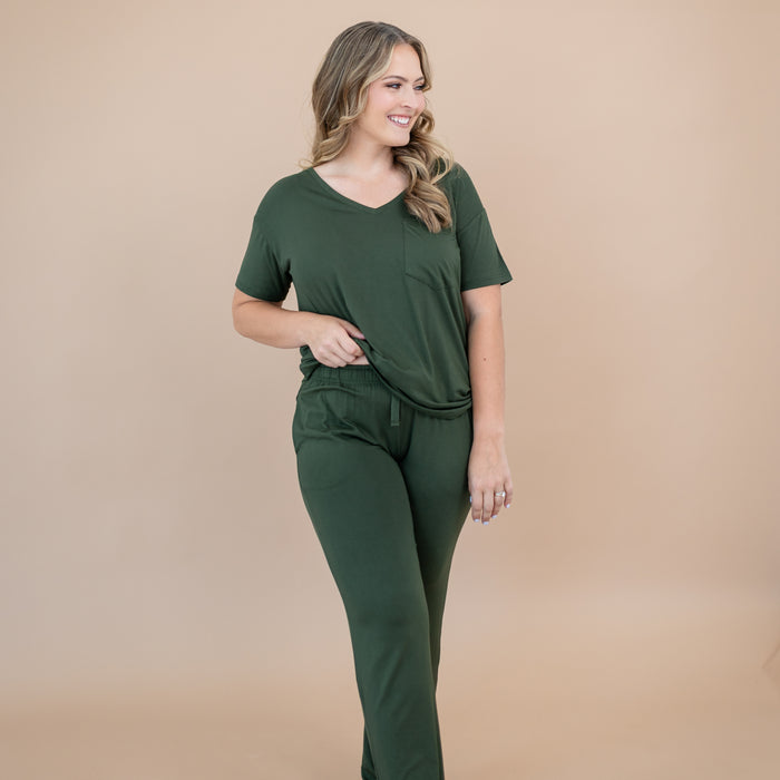 Woman wearing a matching green outfit that includes a bamboo v-neck and lounge pants on a beige background