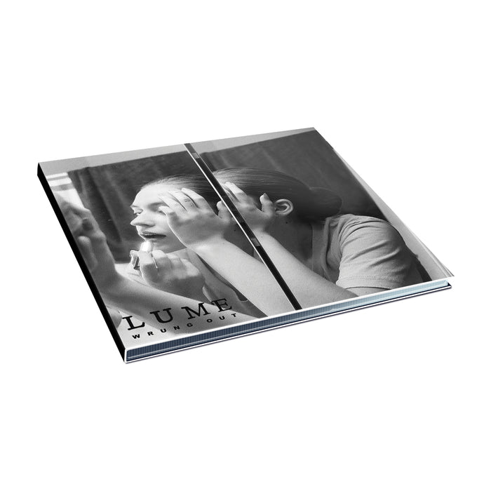 The grayscale album cover for the Lume Wrung Out CD features a woman applying makeup in a mirror. LUME and WRUNG OUT text appears at the lower left, with the tilted image set against a white background.