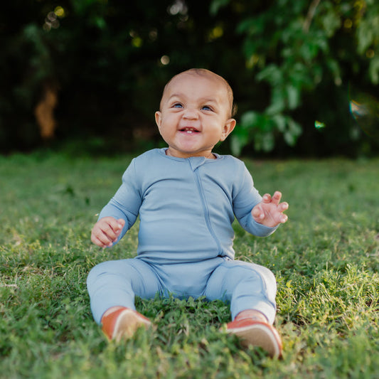 Smiling baby sitting in the grass while wearing a Zippered Romper in Slate